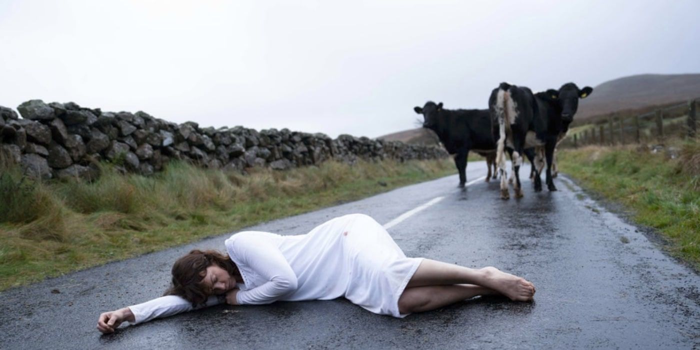 Lorna (Ruth Wilson) yace en una carretera rural frente a unas vacas en The Woman In the Wall.