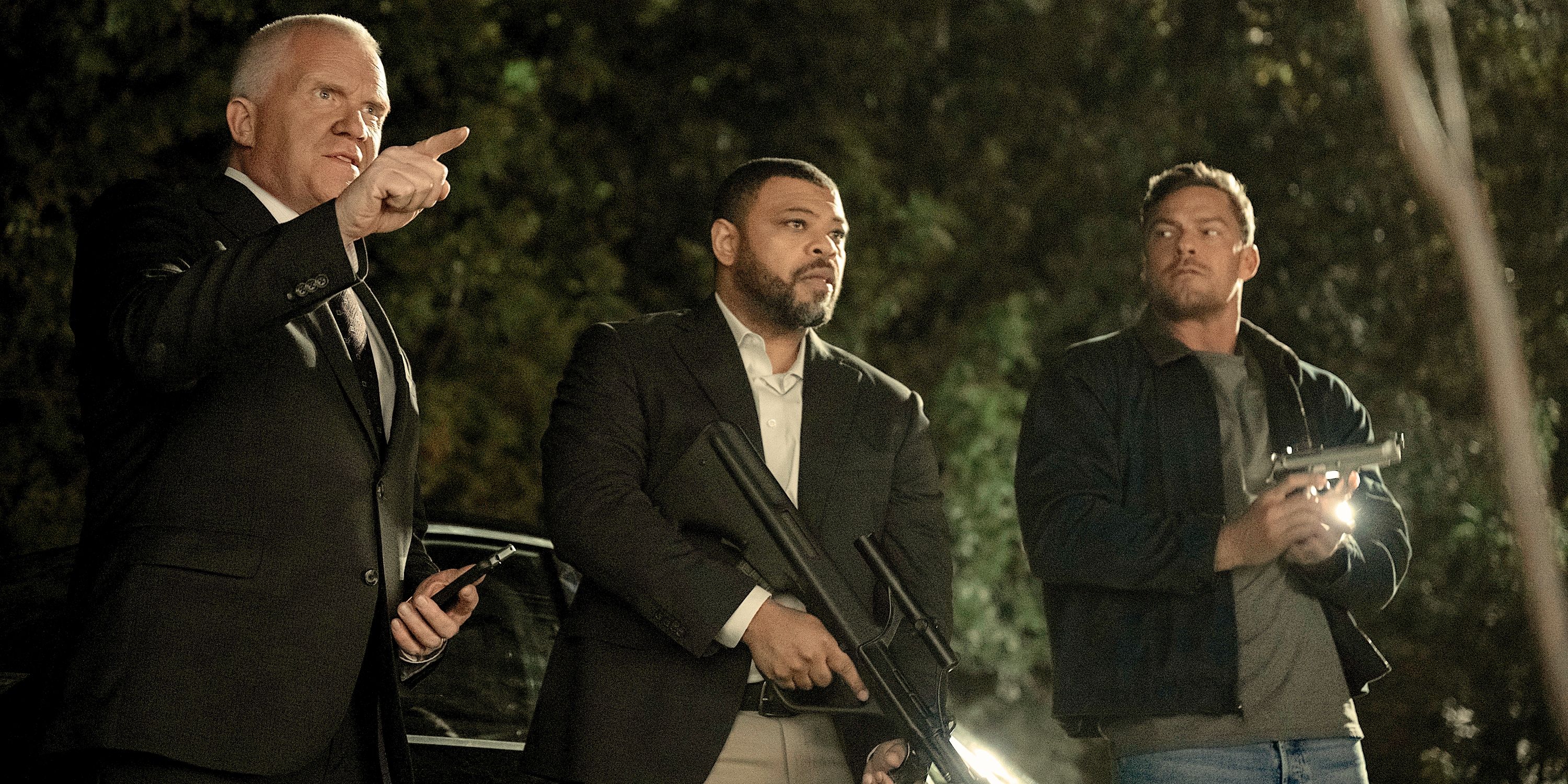 Zachary Beck en traje, Duke con un arma y Reacher en abrigo oscuro