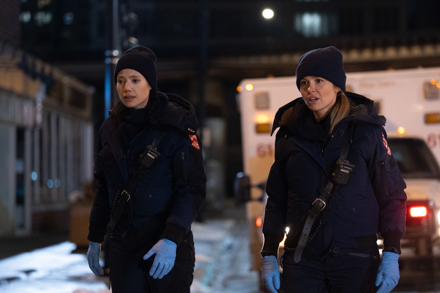 Violet and Novak, wearing paramedic gear, standing outside of an open ambulance on Chicago Fire