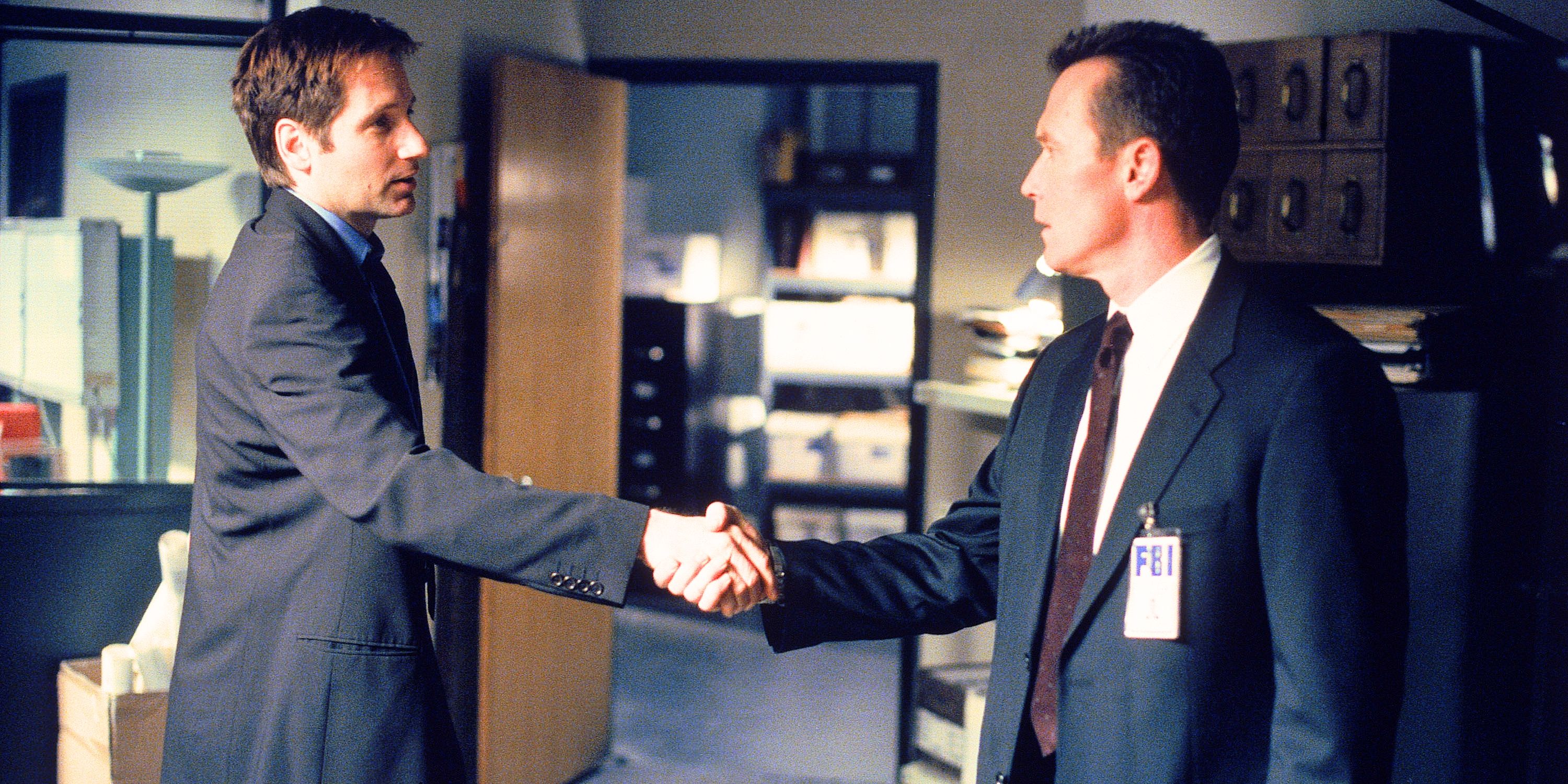 Fox Mulder and John Doggett, both in suits, in profile shaking hands from The X-Files