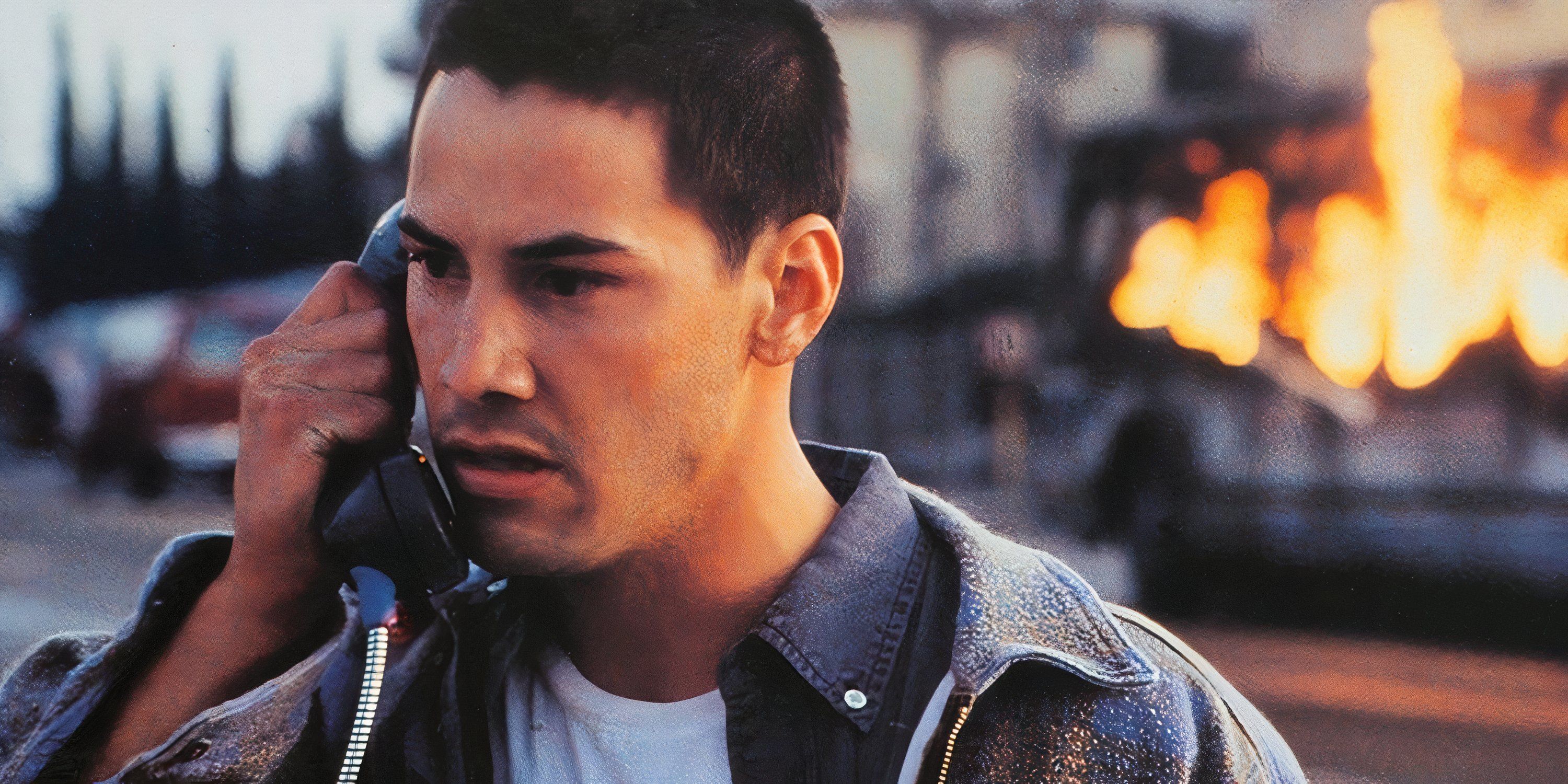 Keanu Reeves talks on the phone while a bus burns behind him in Speed