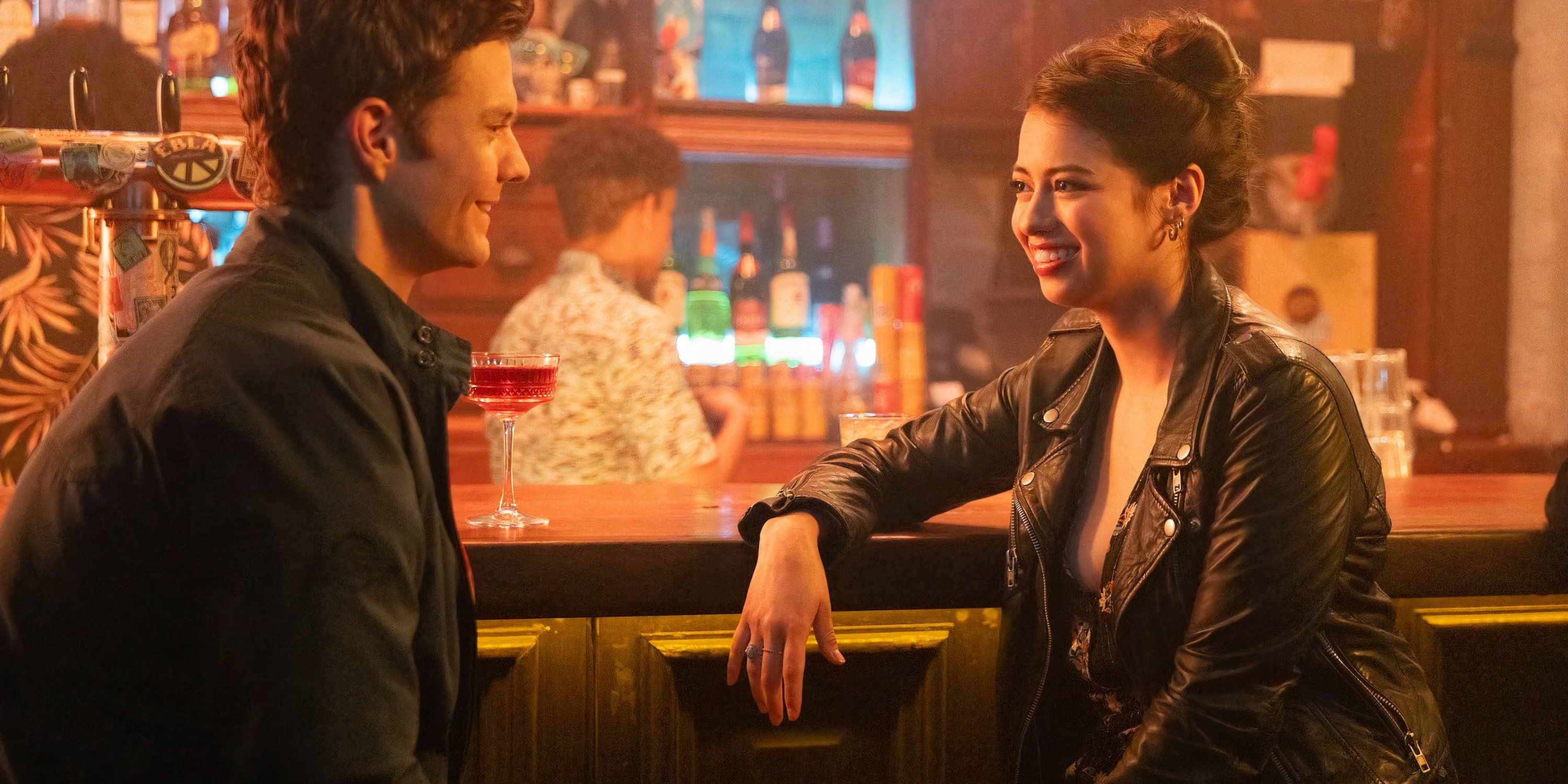 Nathan and Sherry, both wearing black jackets, smile at each other, sitting at a bar in Novocaine