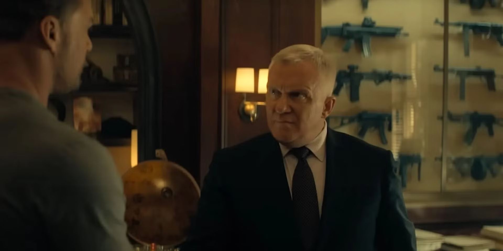 Zachary Beck, wearing a black suit, shakes Reacher's hand with Reacher's back to camera in Reacher