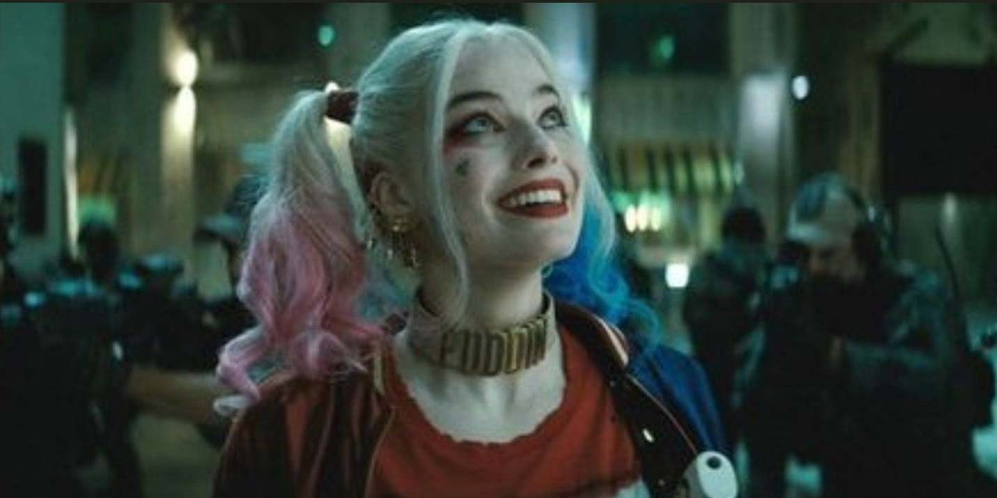 Harley Quinn smiles looking up at something while people point guns at her in Suicide Squad.