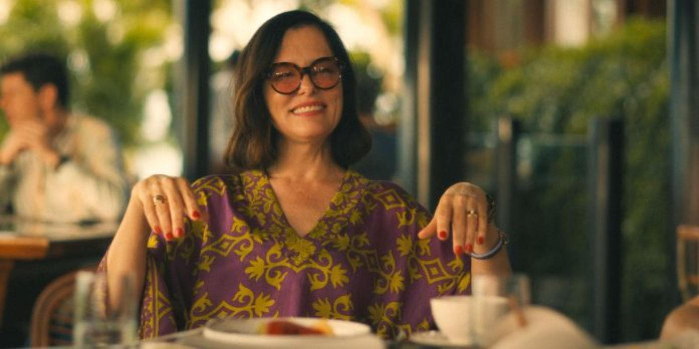 Parker Posey as Victoria Ratliff in The White Lotus with her wrists down in front of her at the table outside.