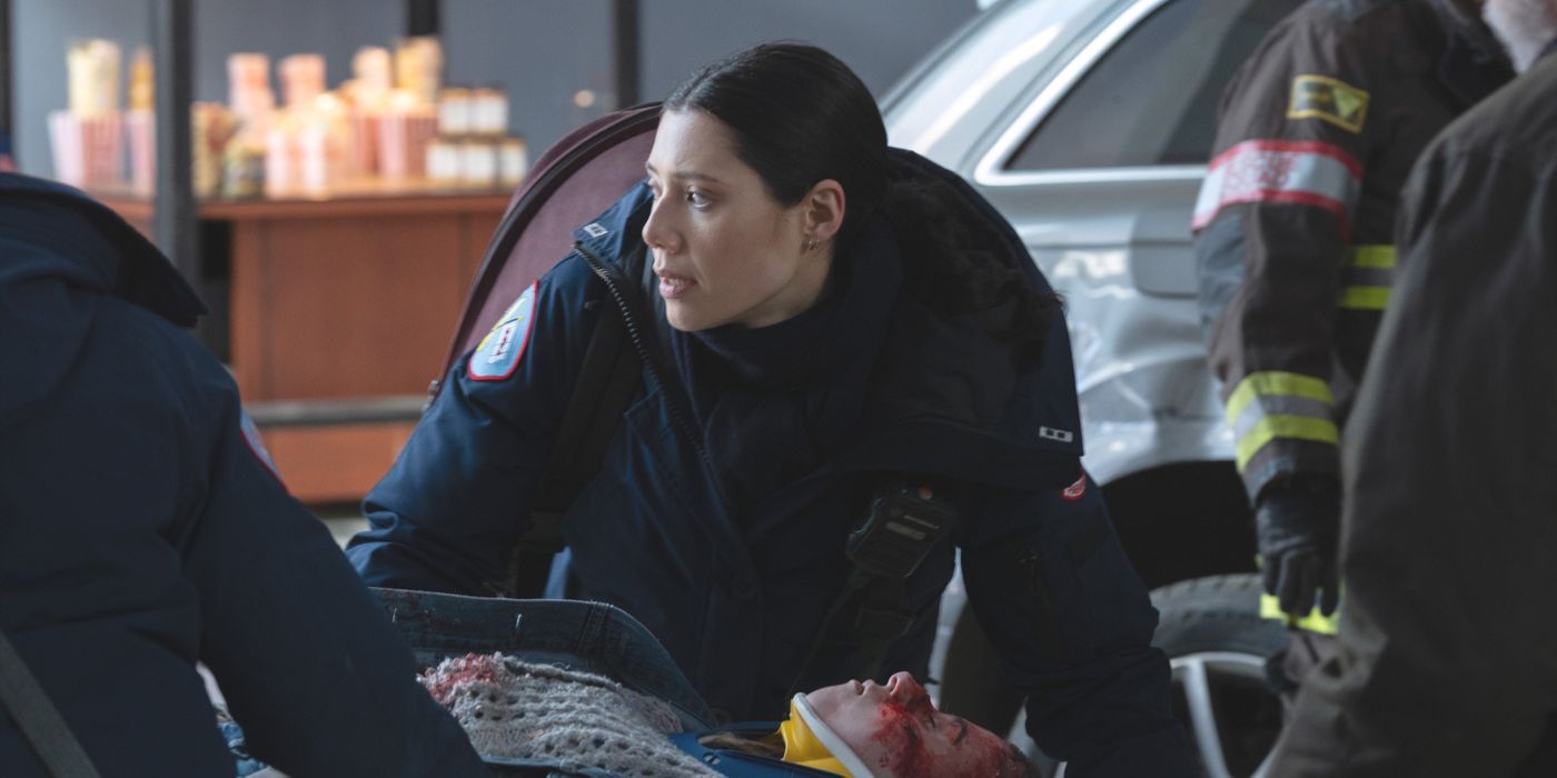 Violet Mikami, wearing a blue jacket, kneels next to a patient at a crash site on Chicago Fire