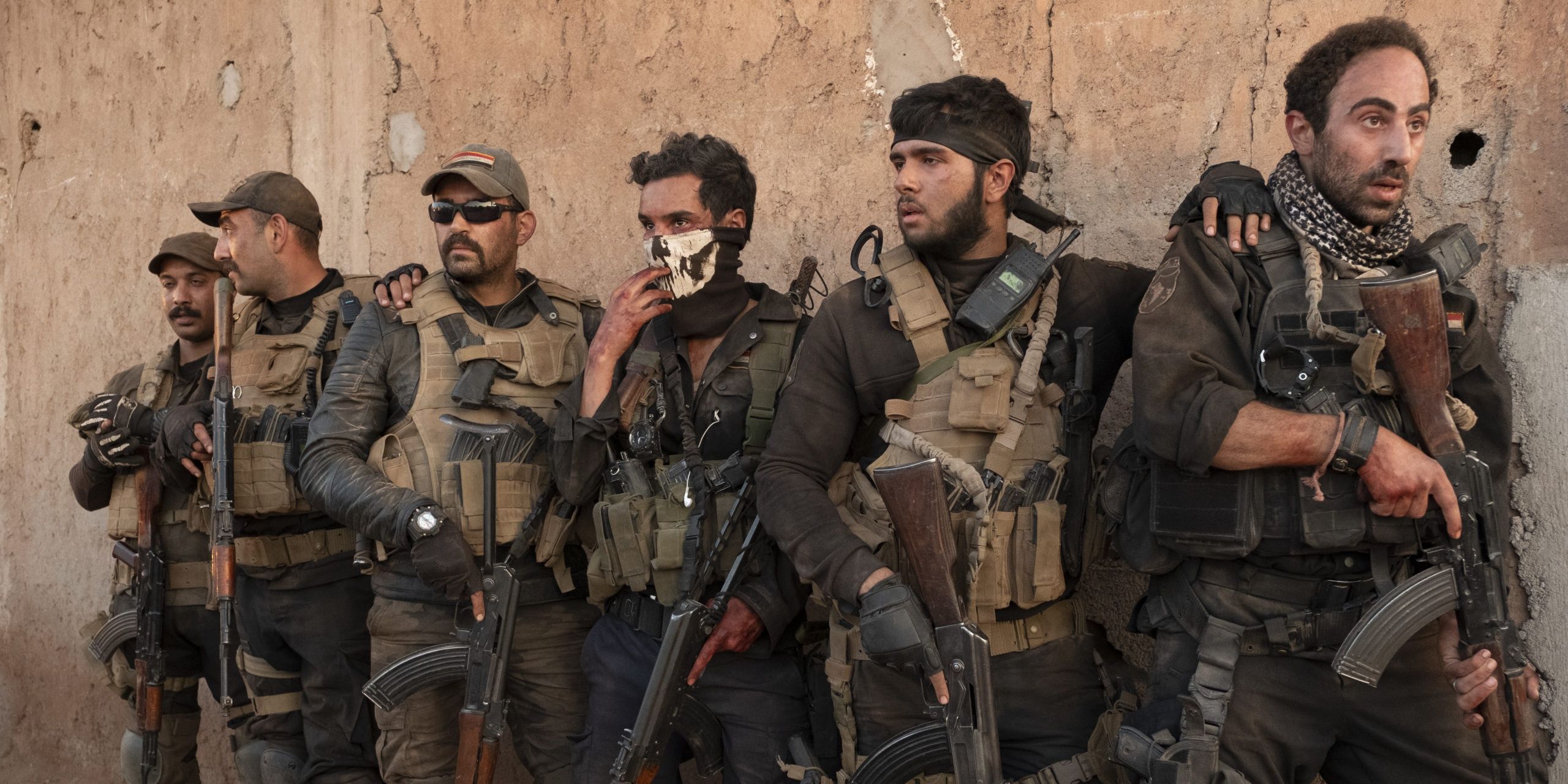 A group of soldier creep from behind a wall of a building in Mosul