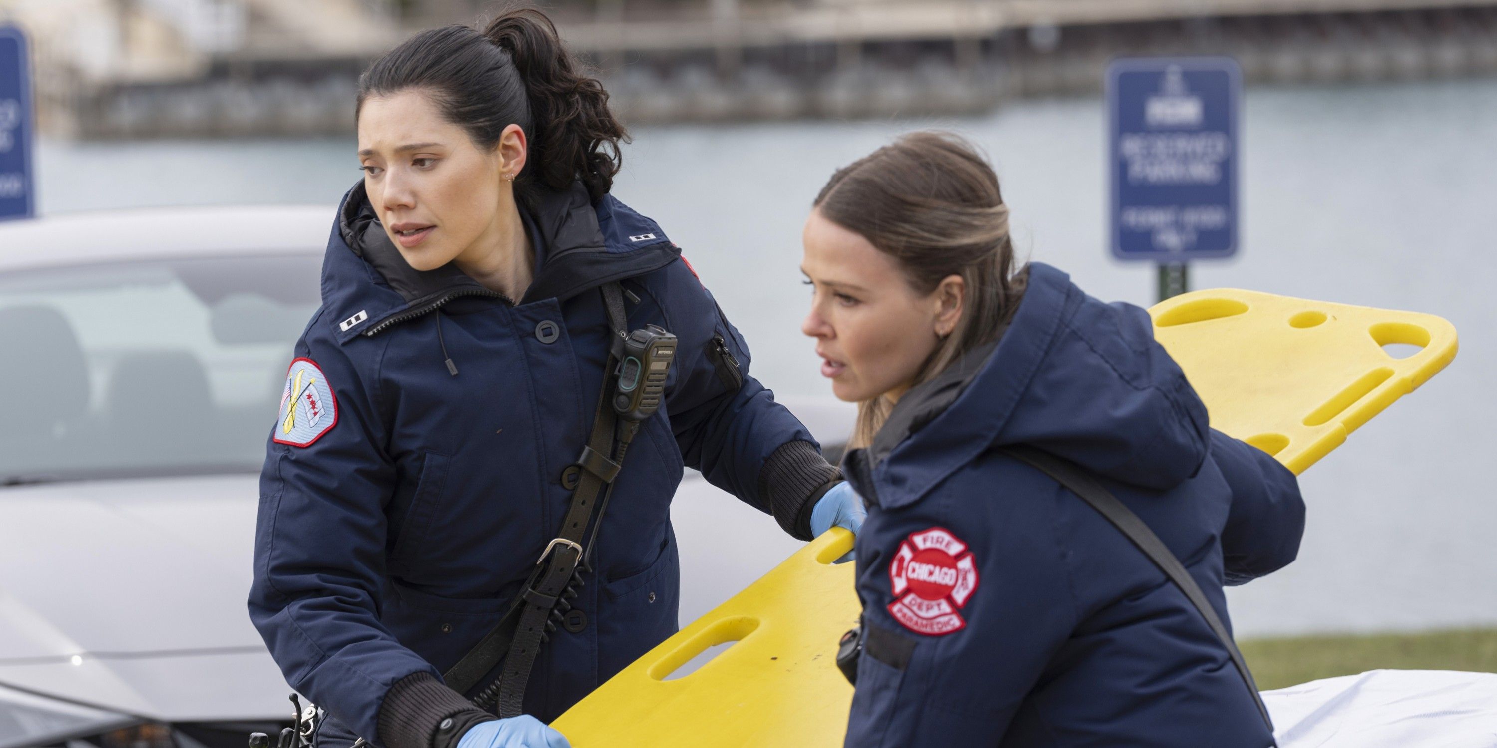 Violet and Novak, both wearing blue paramedic jackets, carry a yellow backboard on Chicago Fire
