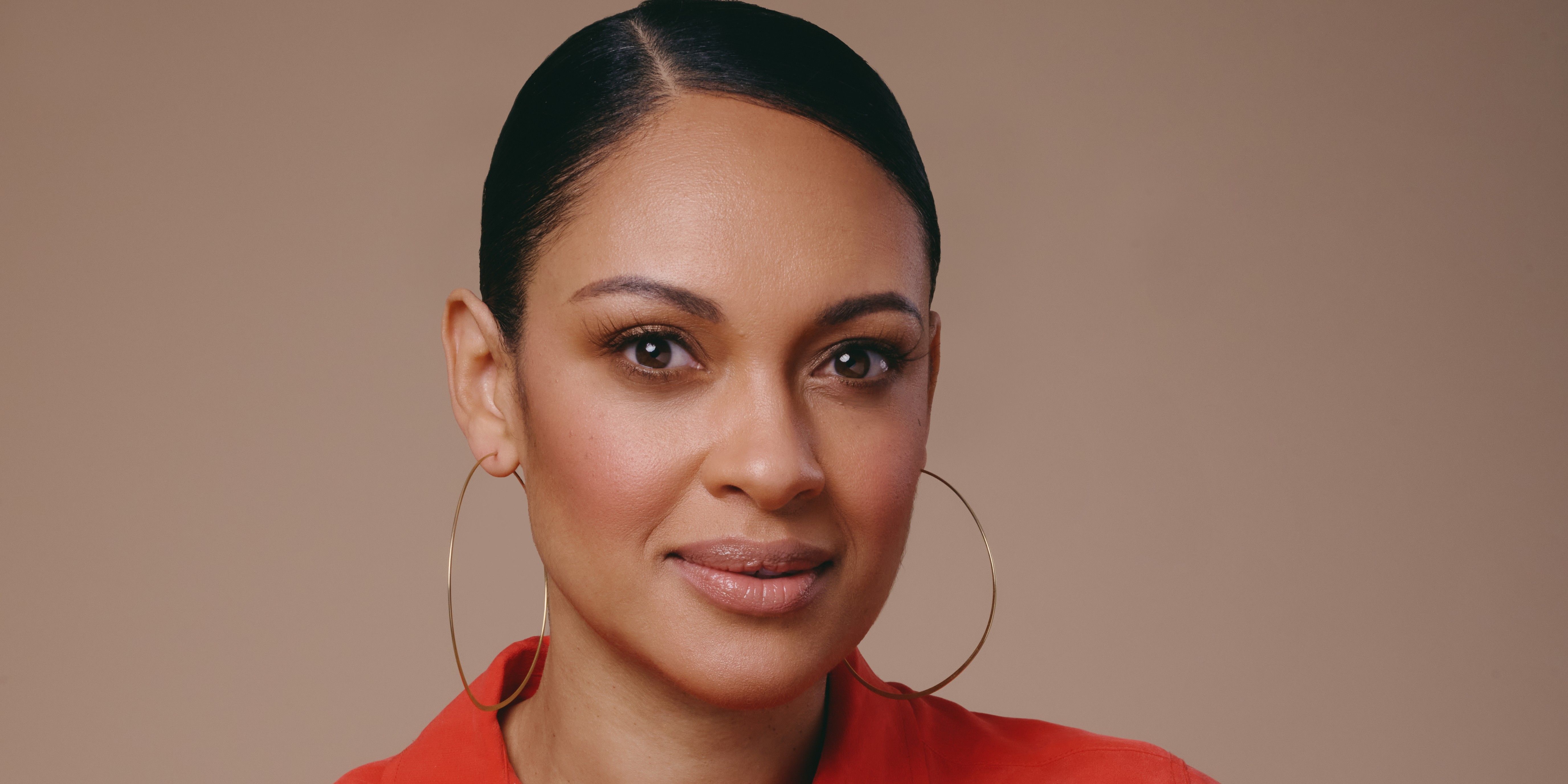 A close-up of actor Cynthia Addai-Robinson in a red blouse on a brown background