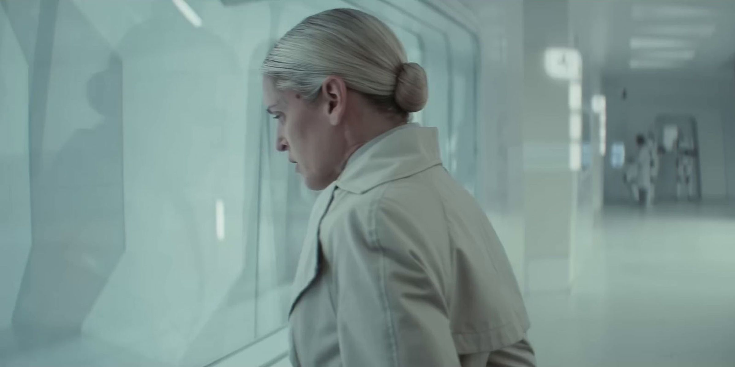 Dedra Meeor in profile wearing a white coat in a white hospital hallway at a window from Andor Star Wars