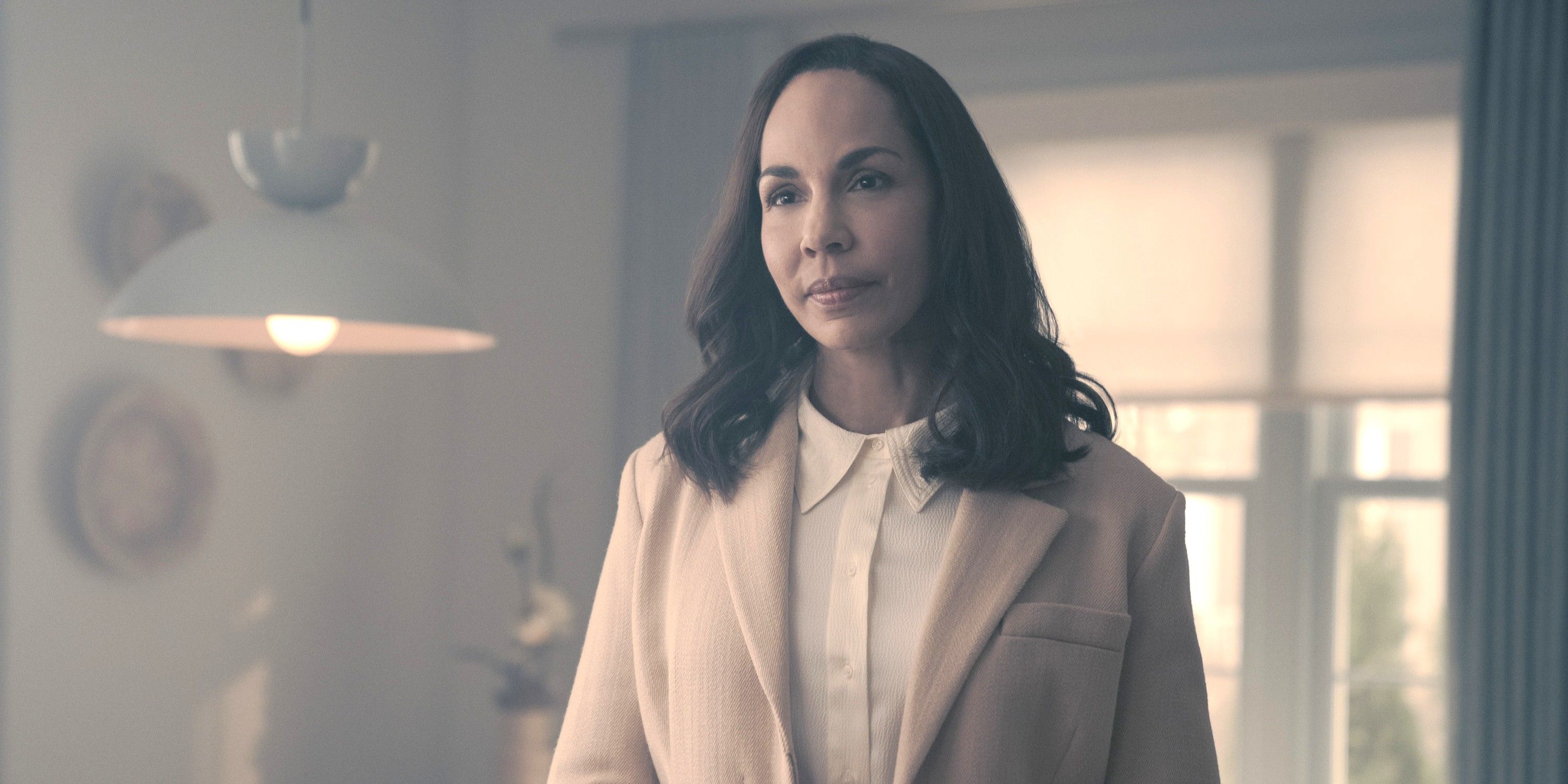 Rita stands wearing a cream blouse and white shirt in the TV show The Handmaid's Tale