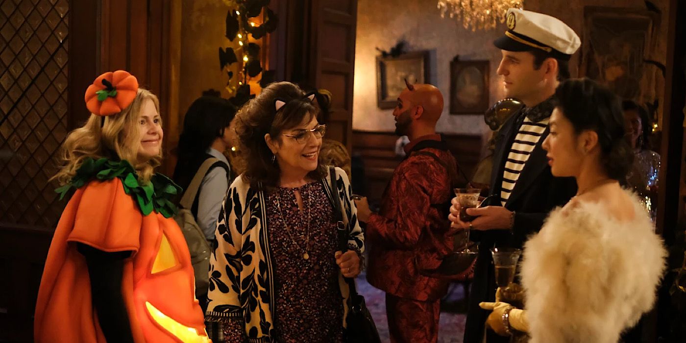 Sam is wearing a pumpkin costume and standing next to Carol who has on cat ears. They talk to two guests.