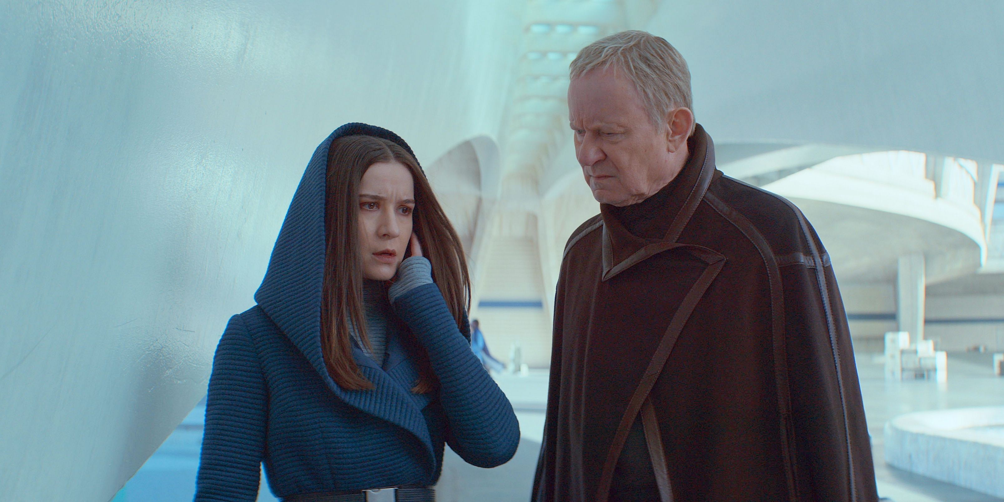 Kleya, hooded in blue, and Luthen Rael, short hair and poncho, in a white alleyway from Andor Star Wars