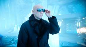 Lex Luthor in a winter coat and mirrored shades, hand grabbing the right side of them, in the fortress of solitude from Superman 2025