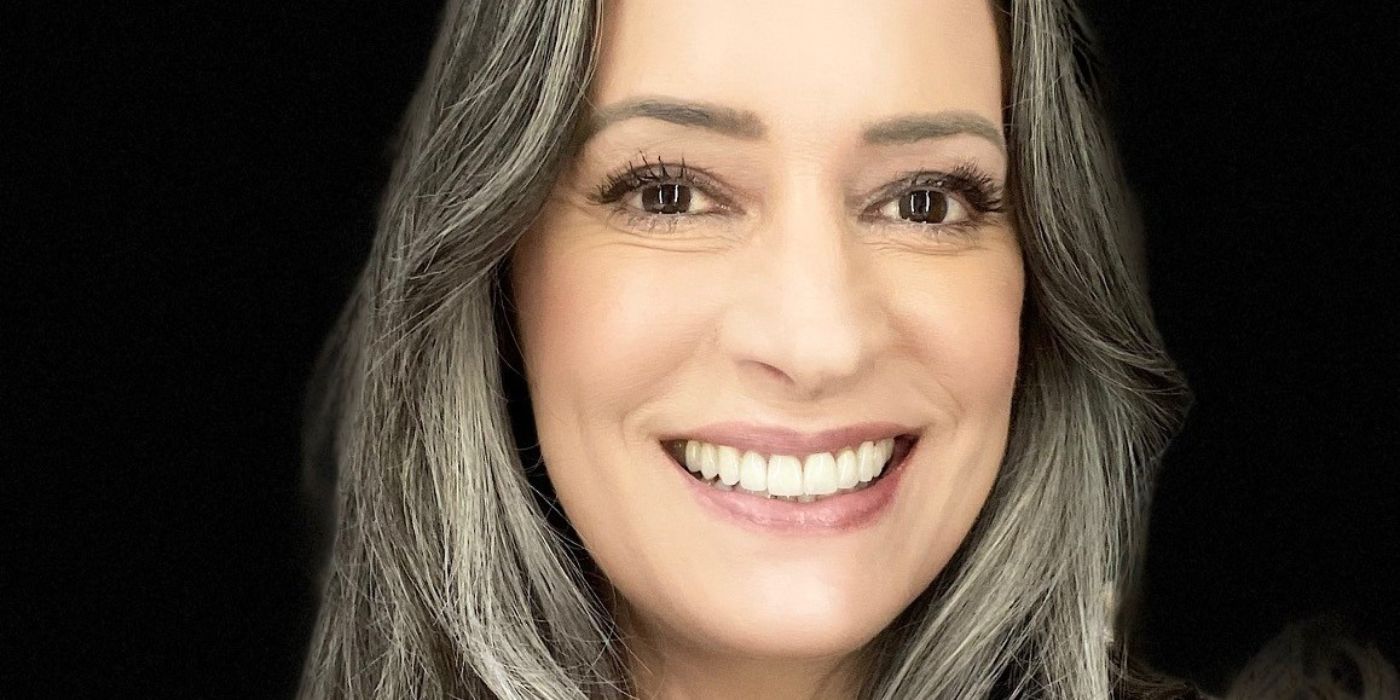 A close-up of actor Paget Brewster smiling on a black background
