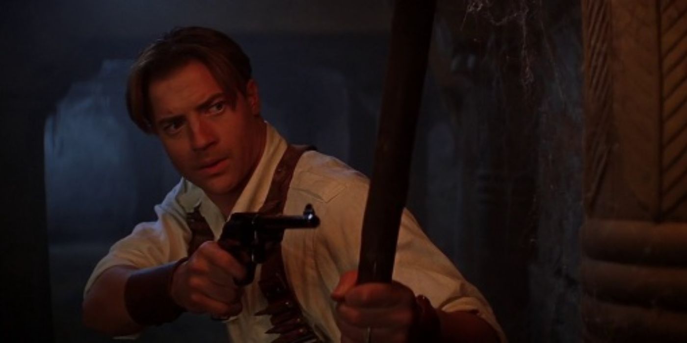 Brendan Fraser como Rick O'Connell señalando con una pistola y sosteniendo una antorcha de La Momia (1999)