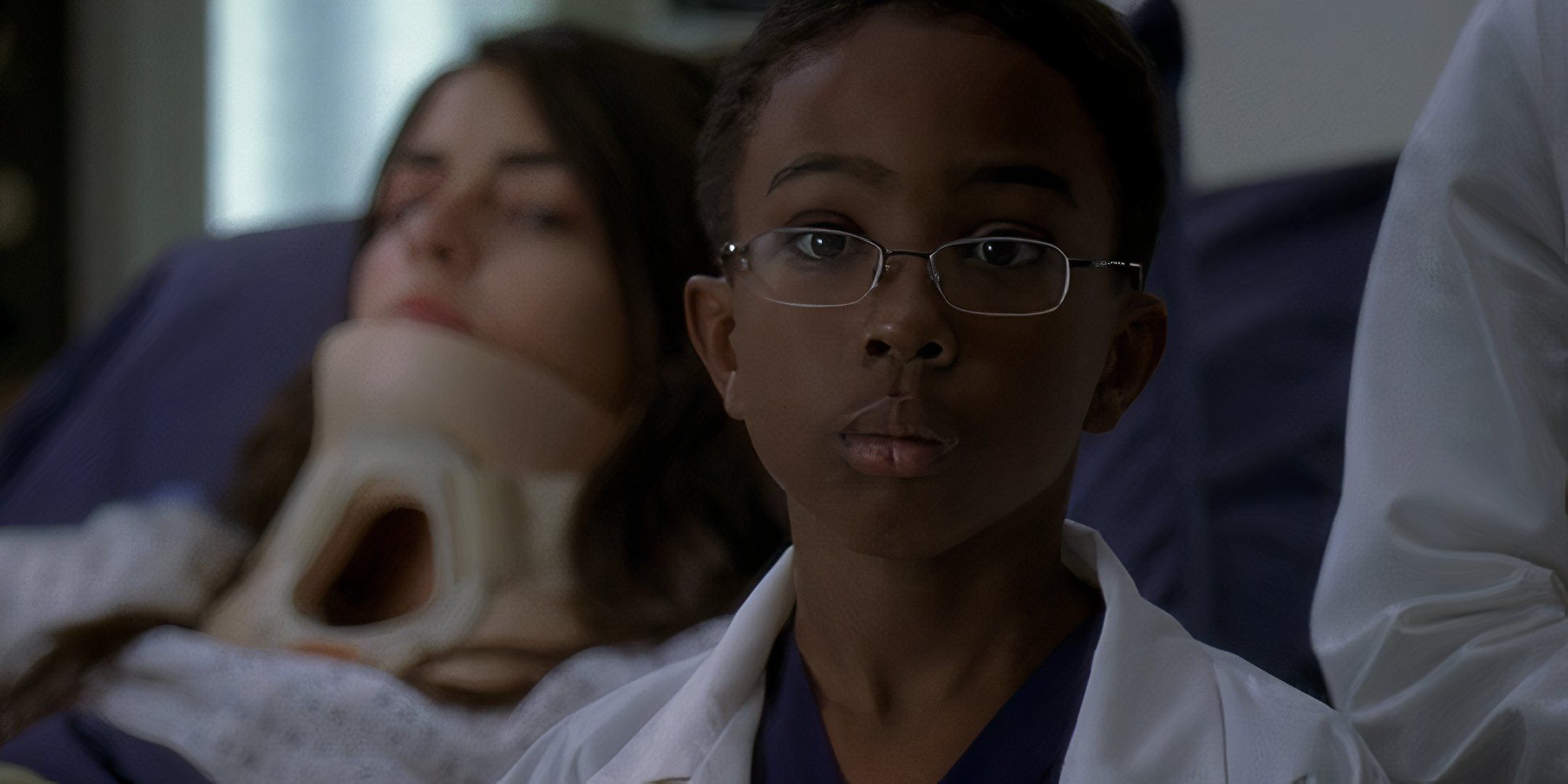 Wallace Anderson wearing his doctor's coat and blue scrubs in front of another patient on "rounds" in Grey's Anatomy.