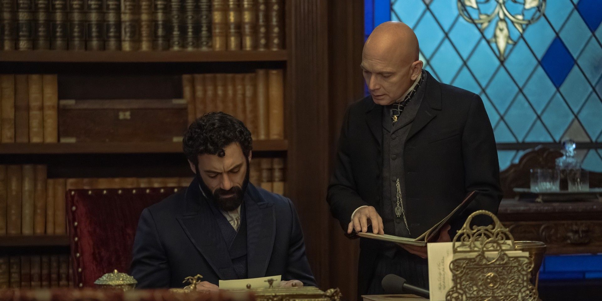 George Russell (Morgan Spector) sitting at a desk with Mr. Watson (Michael Cerveris) in The Gilded Age.