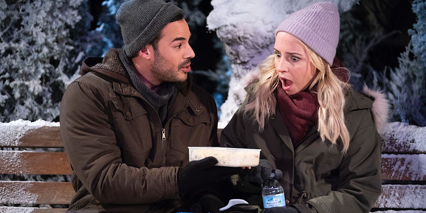 Emilio holds a container of food for Becky as they both sit on a bench in the snow.