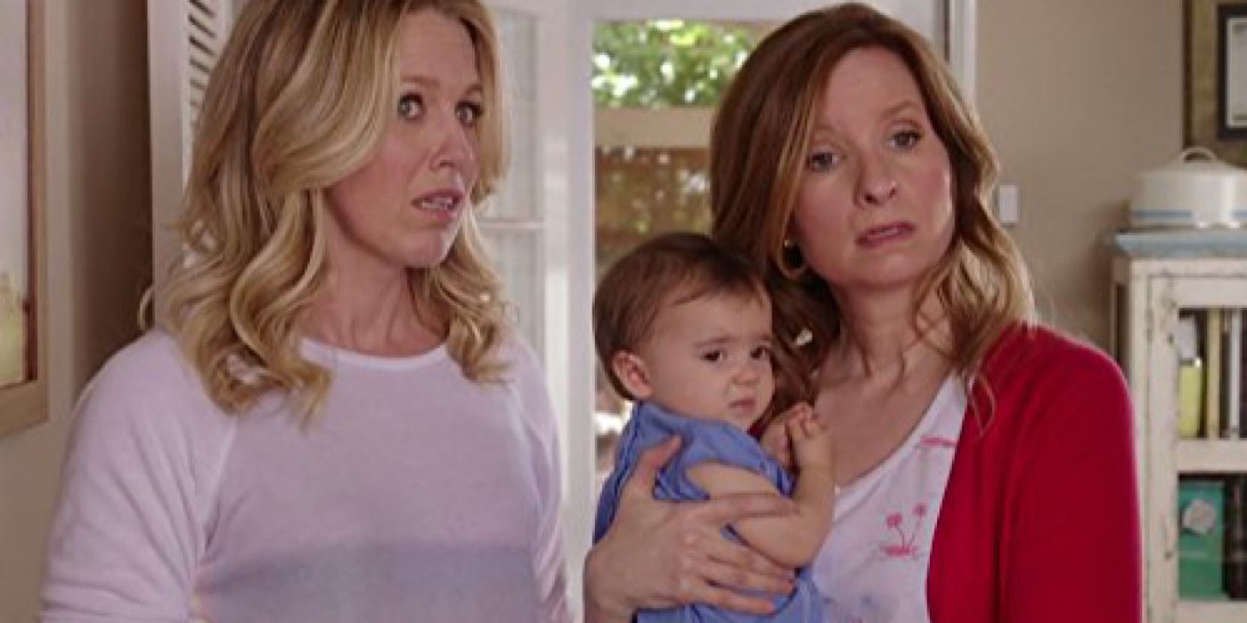 Emma and Maggie stand in the confused house while Maggie carries the baby.