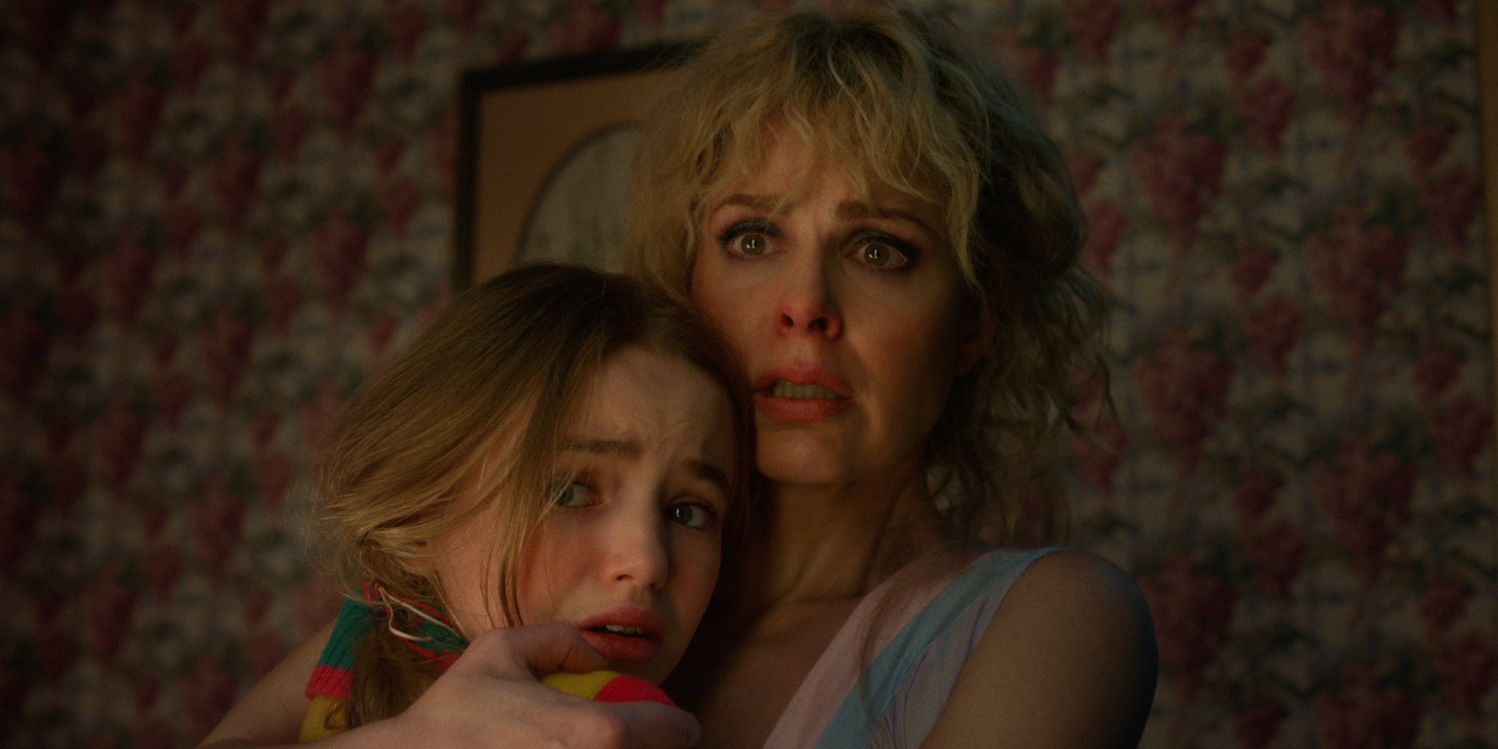 Holly (Nell Fisher) y Karen Wheeler (Cara Buono) besándose y parecen estar asustados en la temporada 5 de Stranger Things.