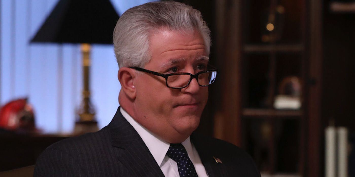 Garrett is wearing a suit and glasses with an American flag pin in the office.