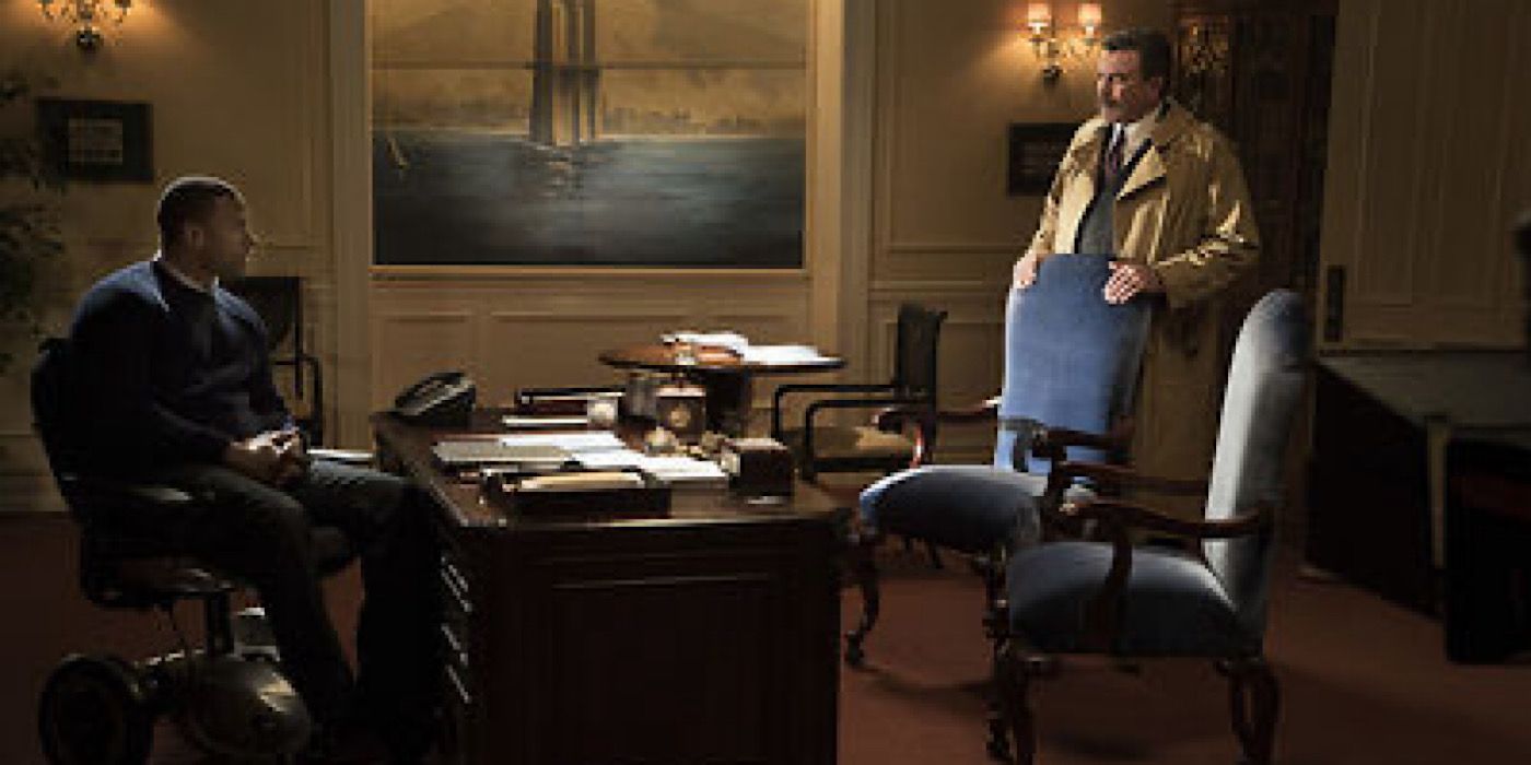 Danny sits in Frank's chair behind his desk as Frank stands behind a guest chair.