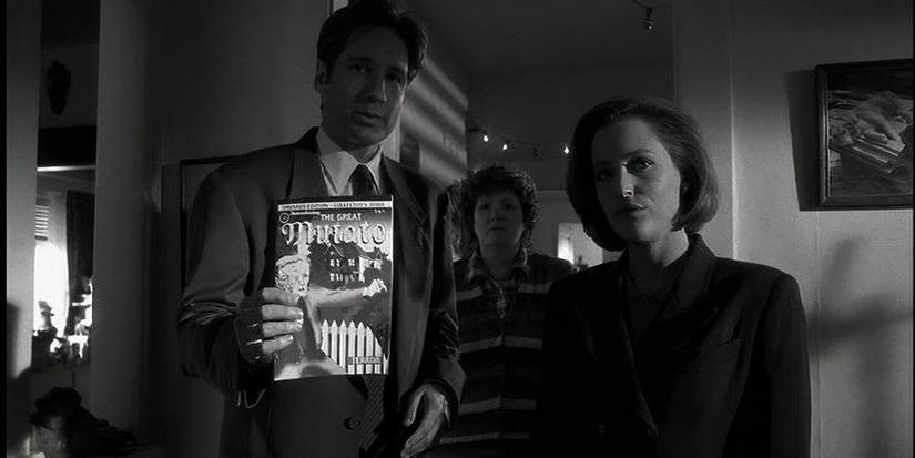 Fox Mulder (David Duchovny) holds the Mutato book while standing next to Dana Scully (Gillian Anderson) in X-Files.