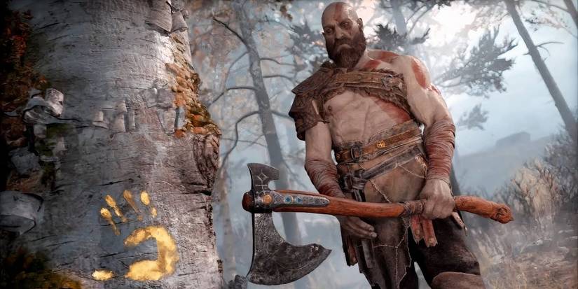 Kratos holding an axe in front of a tree that has a gold handprint on it